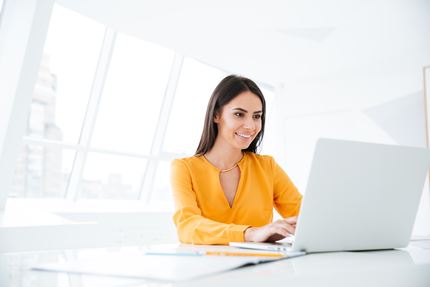 Business woman in orange shirt using laptop computer and sitting by the table in office.